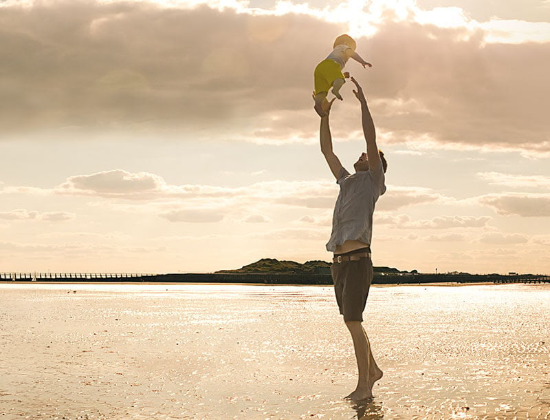 Mann spielt mit Kind am Strand 