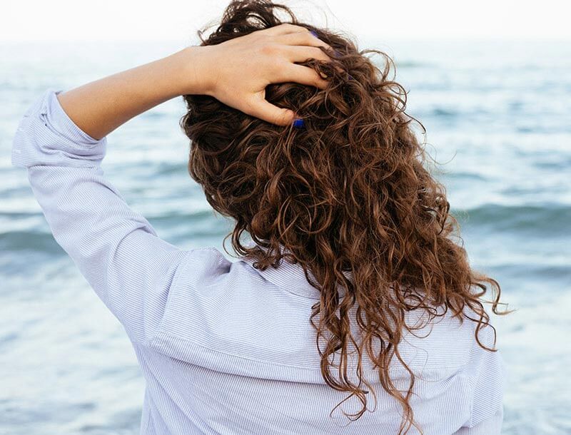 Frau greift sich in die Haare und schaut aufs Meer hinaus